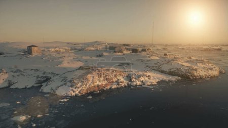 Die Basislandschaft der Antarktis. Drohnenflug aus der Luft. Atemberaubender Panoramablick auf den antarktischen Stützpunkt inmitten schneebedeckter Hügel beim polaren Sonnenuntergang. Siedlung unter rauen Bedingungen.