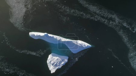 Antarctica iceberg aerial drone view flight. Fast top down. Overview the lone snow white ice mountain, among polar winter ocean water. Beauty of wild untouched nature.