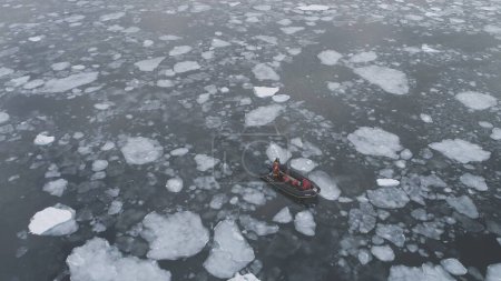 People in rubber inflatable motor boat sail in Antarctic ice. Zodiac in Icebergs, Tracking Aerial Top-Down View. Expedition Transport Exploring Extreme Winter Cold Water. Drone