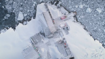 Aerial flight over Vernadsky station in Antarctica. Zoom drone view. Frozen polar ocean surrounding. Ice, snow covered land. Top down overview of Antarctic base. Zooming in.