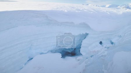Blue ice cave in white glacier on Antarctic Peninsula. Aerial close-up. Antarctica panoramic drone flight view. Snow among polar ice. Cave in iceberg around frozen water. Permafrost. Antarctic