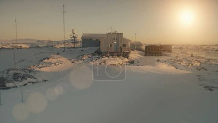 Close-up Vernadsky base and man. Antarctica aerial drone view flight. Fast Antarctic snow covered landscape. Camp, base building with walking man. Sunset polar sky. Permafrost.