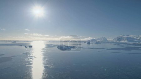 Vuelo aéreo de aviones no tripulados sobre el océano Antártico. Sun Track y Bright Sun Disk. Impresionante paisaje azul blanco polar. Agua fría helada, montañas cubiertas de nieve del continente antártico.