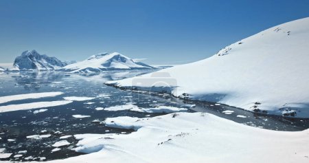 Foto de Increíble belleza de la naturaleza antártica cubierta de nieve. Cordillera, océano polar, glaciar congelado, colonia de pingüinos descansando en el cielo azul de la colina costera. Antártida viajes y exploración. Vuelo panorámico con drones - Imagen libre de derechos