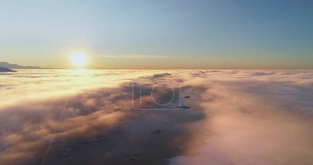 Höhenflug über der morgendlichen Wolkendecke. Sonnenaufgangssonne scheint auf helle Schichten flauschiger Wolken, arktisches Meerwasser und Berggipfel. Natur Hintergrund perfekte Landschaft Tapete