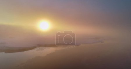 Foto de Vuelo aéreo sobre el cielo de niebla del amanecer en la Antártida. El sol de la mañana brilla a través de las nubes en las montañas nevadas. Panorama épico, sol naranja brillante saliendo. Naturaleza viaje fondo - Imagen libre de derechos