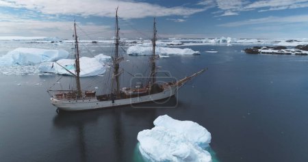 Yacht en bois naviguant parmi les icebergs dans l'océan polaire en Antarctique. Paysage hivernal arctique serein, flots de glace sous le ciel bleu. Exploration, expédition, tourisme, les gens voyagent au pôle Sud. Panorama aérien