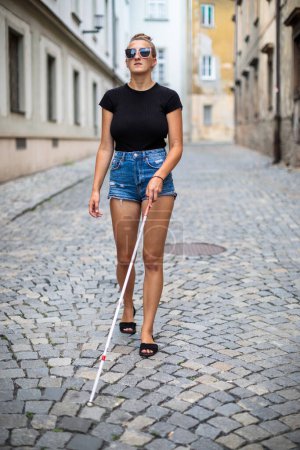 Photo for Blind woman walking on city streets, using her white cane to navigate the urban space better and to get to her destination safely - Royalty Free Image