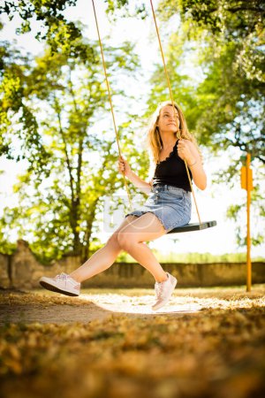 Photo for Carefree woman enjoying summer. Young woman is swinging on a swing in summer park garden. - Royalty Free Image