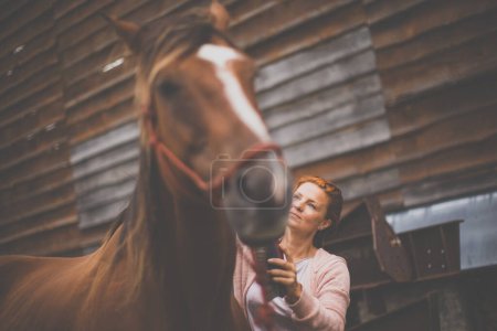 Foto de Mujer guapa, joven, pelirroja con su hermoso caballo, durante su ocio favorito - Imagen libre de derechos