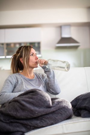 Photo for Midlle aged woman at home with a bottle of strong alcohol in her hands - Royalty Free Image