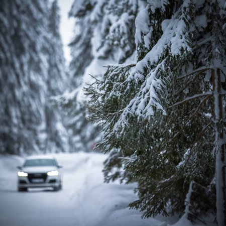 Téléchargez les photos : Voiture sur une route enneigée d'hiver au milieu des forêts en utilisant ses capacités de quatre roues motrices pour traverser la neige - en image libre de droit