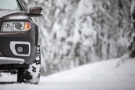 Foto de Coche en una carretera nevada de invierno en medio de los bosques, utilizando sus capacidades de tracción a las cuatro ruedas para atravesar la nieve - Imagen libre de derechos