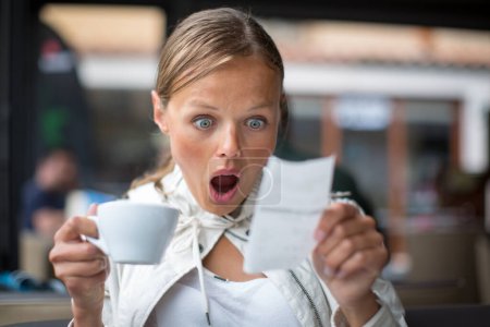 Jolie, jeune femme déroutée avec la facture dans un café / restaurant