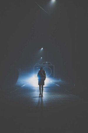 Foto de Carretera oscura con una mujer caminando por el medio. chica solitaria mujer de pie en el estacionamiento oscuro en la noche oscuridad cerca de detener el tráfico señal de tráfico no conducir pensando sufrir sentir estrés depresión desesperación (color tonificado imagen) - Imagen libre de derechos