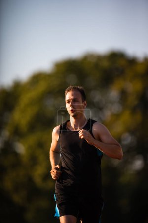 Téléchargez les photos : Beau jeune coureur jogging en plein air lors d'une belle soirée d'été - en image libre de droit