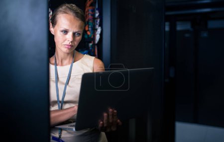 Photo for IT engineer standing before working server rack doing routine maintenance check and diagnostics using laptop - Royalty Free Image