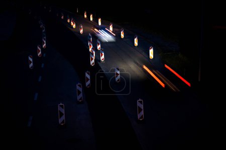 Téléchargez les photos : Voitures sur une route avec travaux routiers. Il travaille sur la route. Circulation nocturne. - en image libre de droit