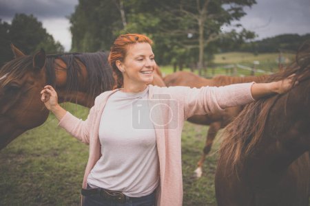Téléchargez les photos : Jolie, jeune, rousse femme avec son beau cheval, pendant ses loisirs préférés - en image libre de droit