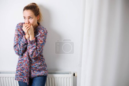 Téléchargez les photos : Femme froide et déprimée d'âge moyen à la maison se sentant triste, seule, anxieuse de la hausse des prix de l'énergie (image couleur tonique) - en image libre de droit