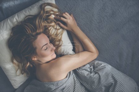 Téléchargez les photos : Jolie, jeune femme dormant dans son lit tard le matin un week-end pour compenser le manque de sommeil - en image libre de droit