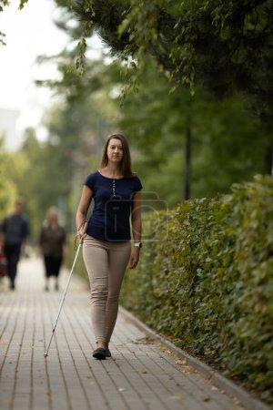 Téléchargez les photos : Jeune femme ayant une déficience visuelle marchant dans les rues de la ville, en utilisant sa canne blanche - en image libre de droit