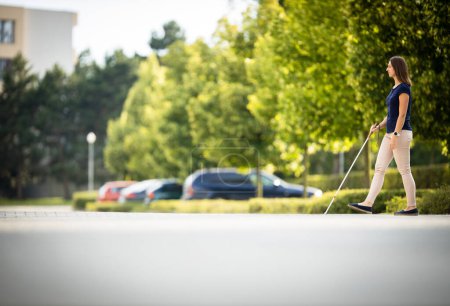 Foto de Mujer joven con discapacidad visual caminando por las calles de la ciudad, usando su bastón blanco - Imagen libre de derechos