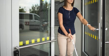Photo for Young woman with impaired vision walking on city streets, using her white cane to navigate the urban space better and to get to her destination safely - Royalty Free Image