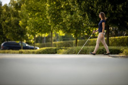 Photo for Young woman with impaired vision walking on city streets, using her white cane to navigate the urban space better and to get to her destination safely - Royalty Free Image