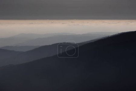 Foto de Paisaje atmosférico montañoso de altas montañas en espesa niebla en clima lluvioso, panorama de cimas montañosas en espesas nubes, amanecer en las montañas a principios de primavera. - Imagen libre de derechos