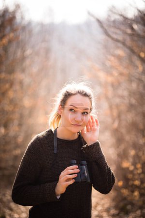 Photo for Young woman with binoculars outdoors on fall day. Enjoying the outdoors. Listening to bird voices. - Royalty Free Image