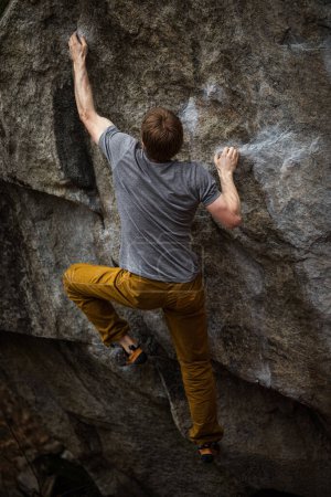 Photo for A rock climber climbing on a boulder rock outdoors. Group of friends involved in sports outside. - Royalty Free Image