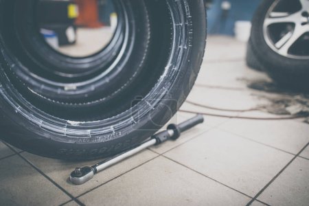 Téléchargez les photos : Mécanicien automobile changer les pneus d'une voiture dans un atelier de réparation / garage de voiture (peu profonde DOF / image couleur tonique) - en image libre de droit
