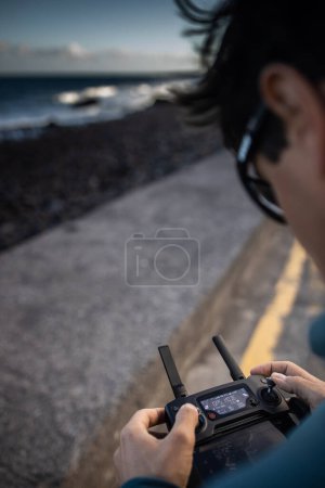 Téléchargez les photos : Pilote de drone en action, prenant des photos aériennes et capturant des images de vagues s'écrasant sur une plage - en image libre de droit