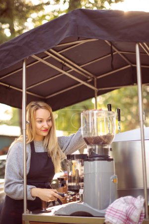 Photo for Female barrista making coffee for clients in a mobile coffee stand outdoors in a city - Royalty Free Image