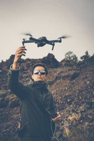 Téléchargez les photos : Jeune homme avec un drone à l'extérieur, volant dans des conditions venteuses - en image libre de droit