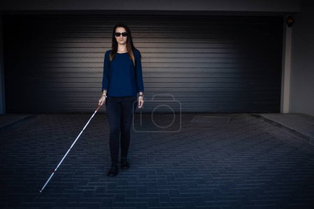 Foto de Mujer ciega caminando por las calles de la ciudad, usando su bastón blanco para navegar mejor por el espacio urbano y llegar a su destino con seguridad - Imagen libre de derechos
