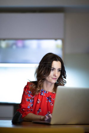 Photo for Pretty, mid-aged woman using her laptop in the evening at home - Royalty Free Image