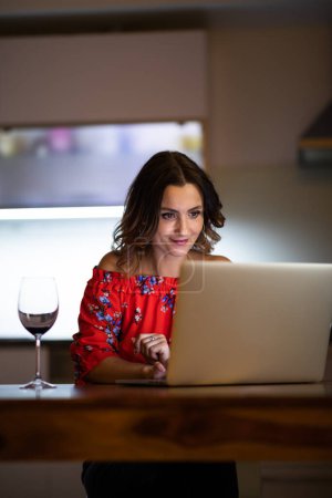 Foto de Mujer bonita y de mediana edad que tiene una cena virtual de degustación de vinos en línea utilizando el ordenador portátil con amigos - Imagen libre de derechos
