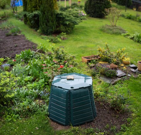 Téléchargez les photos : Poubelle de compostage extérieure pour le recyclage des déchets organiques de cuisine et de jardin dans un joli jardin luxuriant - en image libre de droit