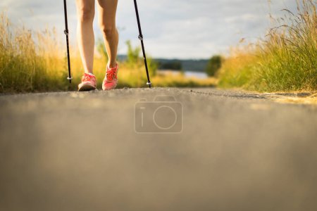 Foto de Piernas sanas de una mujer joven y bonita que camina afuera en un hermoso día de verano. Caminar nórdico con postes. - Imagen libre de derechos