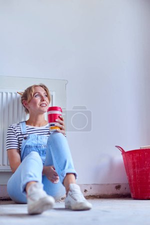 Mujer decoración habitación en casa sentado en el piso tomando un descanso con bebida caliente en taza reutilizable
