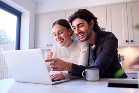 Couple At Home Looking At Laptop On Counter In Kitchen Together Poster 649424876