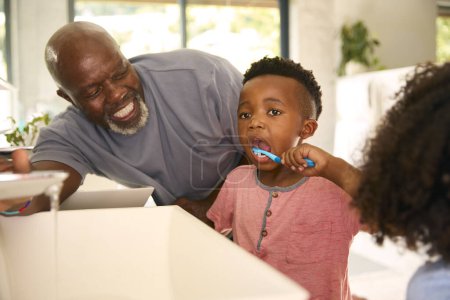 Großvater hilft Enkeln beim Zähneputzen im Badezimmer zu Hause vor dem Bett