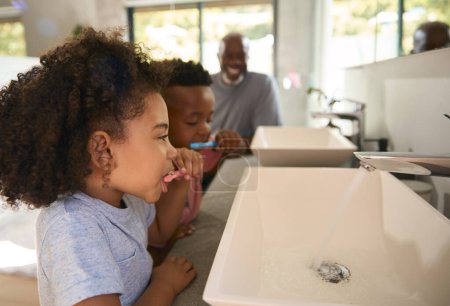 Abuelo ayudando a sus nietos a cepillarse los dientes en el baño en casa antes de acostarse