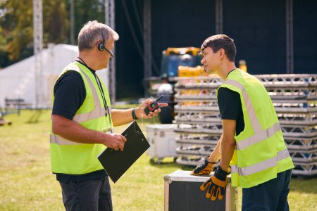 Equipo de producción masculino con auriculares que configuran el escenario al aire libre para el festival de música o el concierto