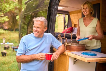 Senior Couple Enjoying Camping In Countryside Relaxing Inside RV And Doing Chores Together