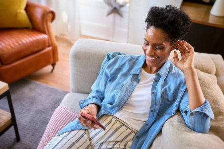 Mature Woman Relaxing On Sofa At Home Looking At Mobile Phone