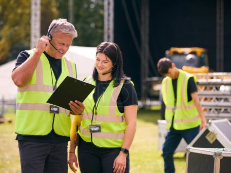 Production Team Talking On Headsets Setting Up Outdoor Stage For Music Festival Or Concert