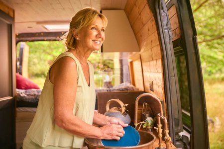 Senior Woman Enjoying Camping In Countryside Relaxing Inside RV And Doing Chores
